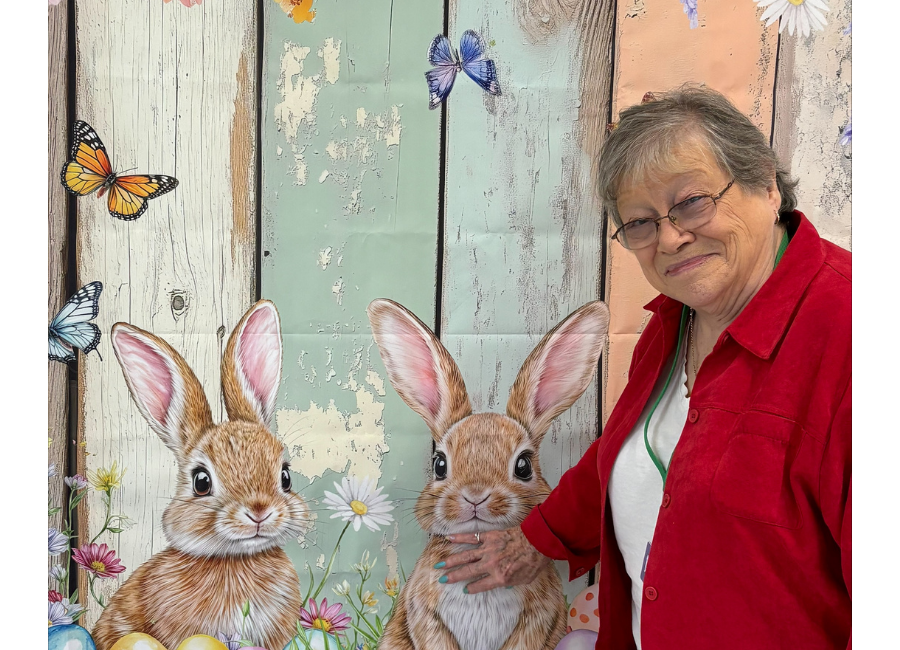 Anna Case in a red shirt standing beside a mural with bunnies and butterflies at a PACE center